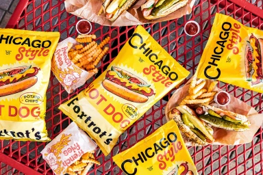Overhead view of Foxtrot Chicago Style hot dog packaging, french fries, and condiment cups on a red wire mesh table.