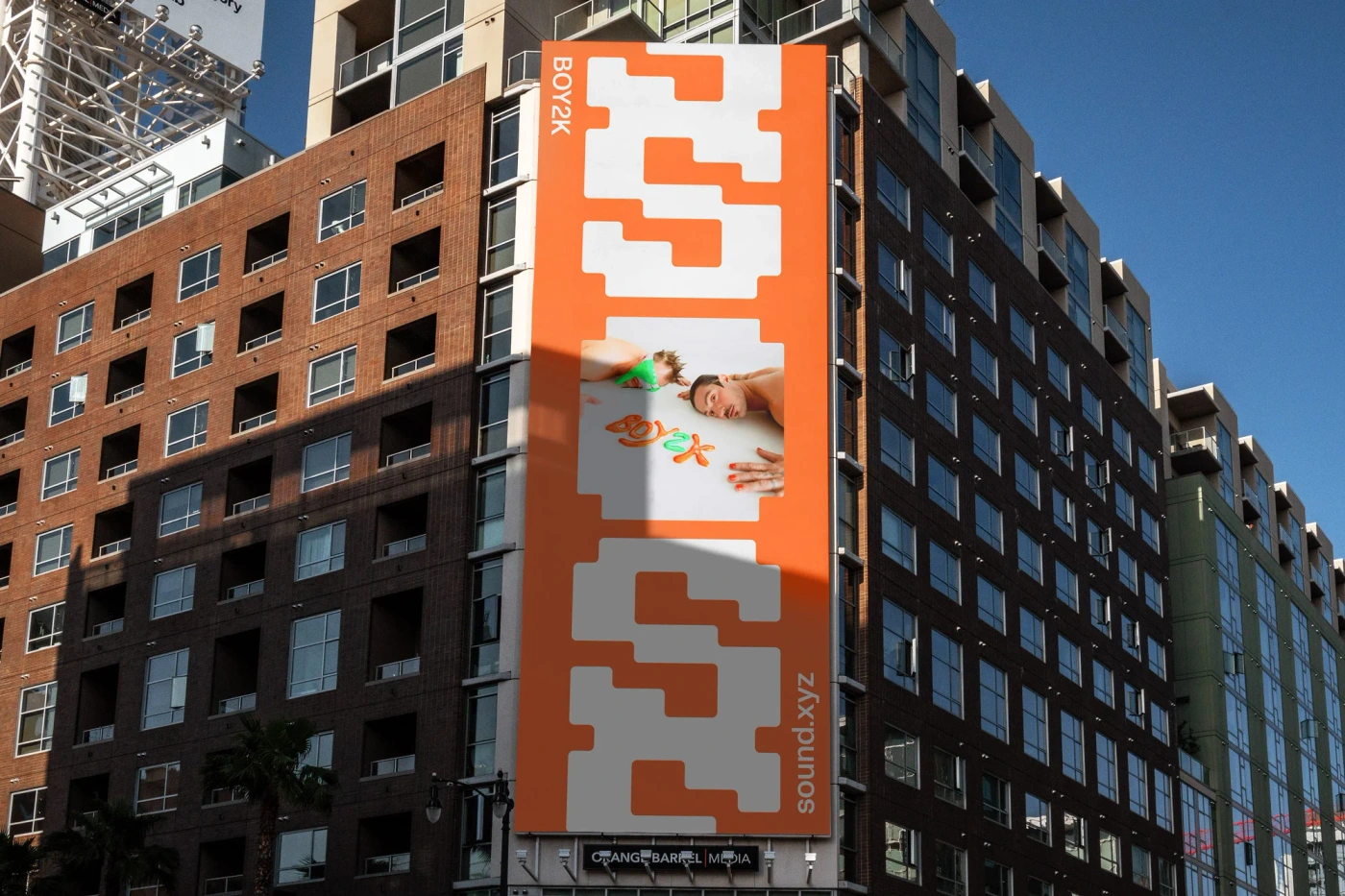 Large orange and white billboard on a brick apartment building exterior under clear sky