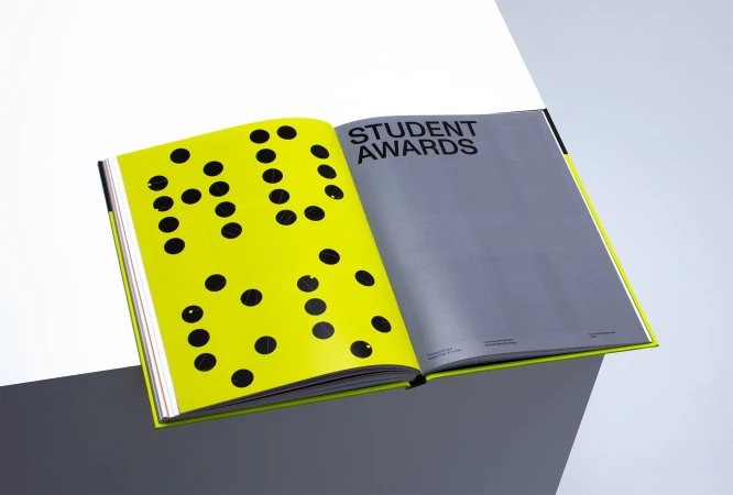 Open book displaying graphic design and typography on a geometric white and gray background, showcasing student award work.