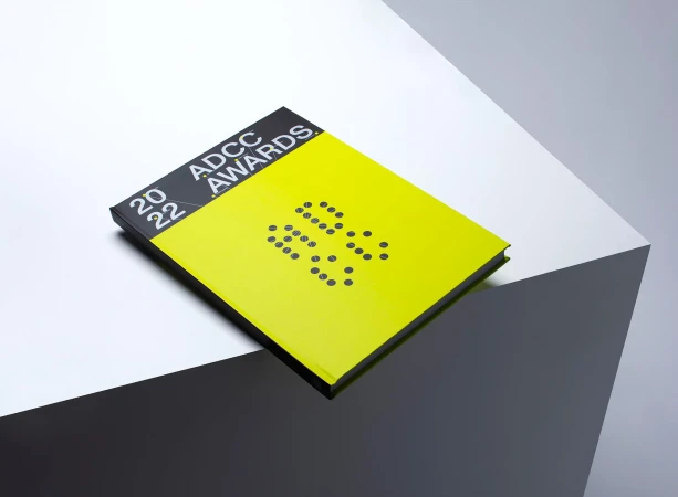 ADCC Awards 2022 book with a neon yellow cover featuring a simple dot graphic in front of a geometric white and grey background.