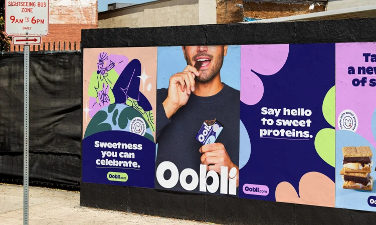 Outdoor Oobli advertisement featuring a smiling man eating a protein bar, a colorful graphic design, and images of sweet protein snacks.