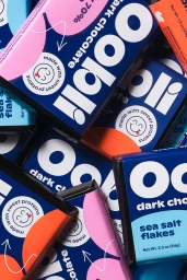 Close-up overhead shot of multiple colourful Oobli dark chocolate packaging boxes stacked together.