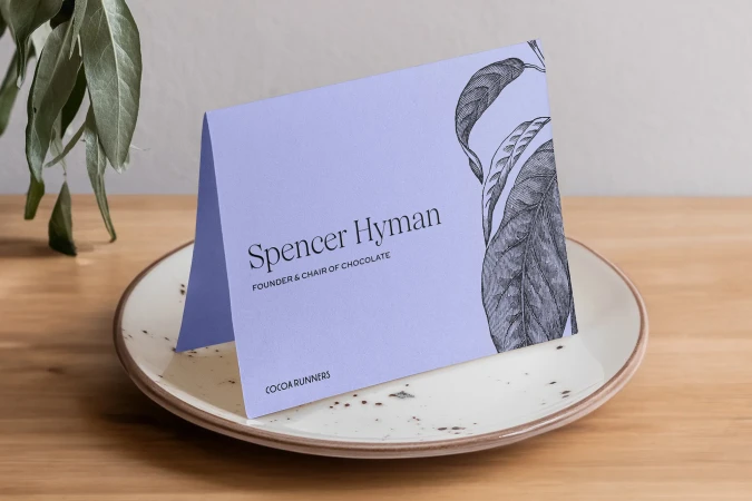 Elevated shot of a presentation card on a speckled plate, with a black and white botanical design and soft, indirect lighting.