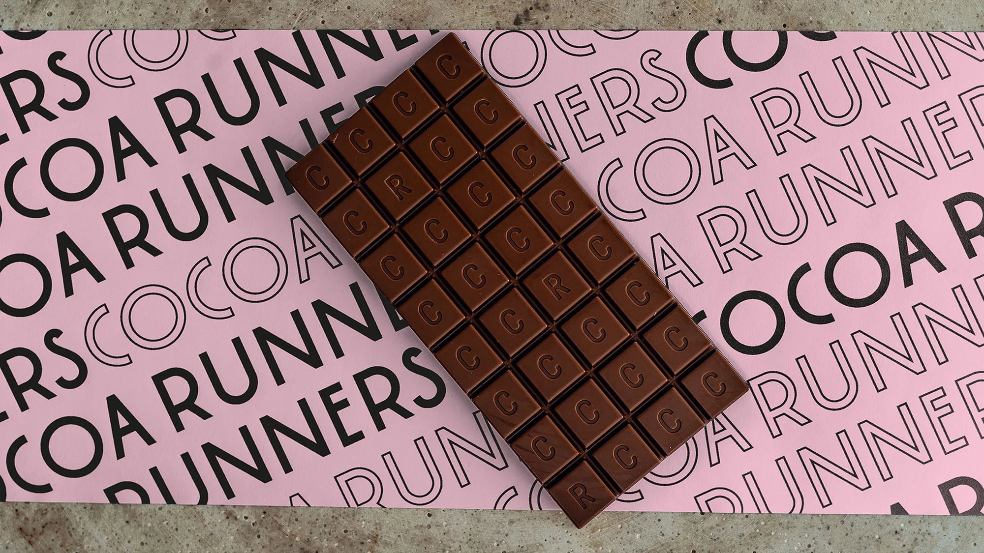 Overhead shot of milk chocolate bar on pink paper with Cocoa Runners text pattern, studio shot, commercial food photography.