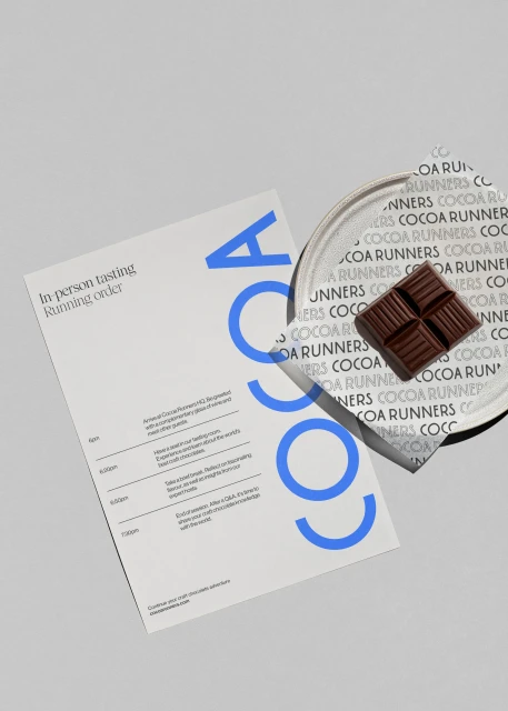 Close-up of dark chocolate squares on a patterned plate next to a program for a Cocoa Runners in-person tasting event.