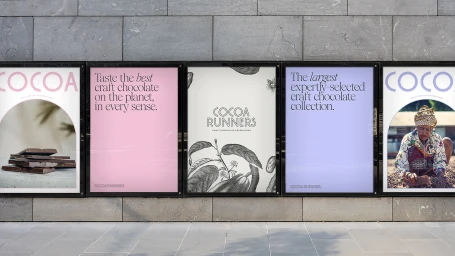 Five framed advertising posters mounted on a grey stone wall displaying typography and botanical illustrations for Cocoa Runners.