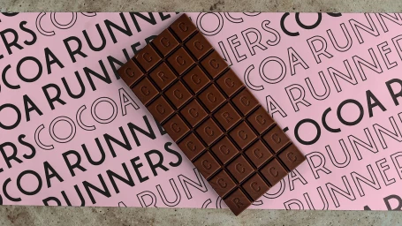Chocolate bar with embossed lettering resting on a pink branded paper background with black typography