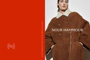 Model wearing a brown shearling coat with a white collar against a light background beside a solid red panel
