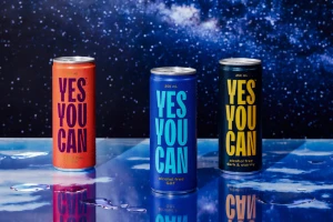 Three beverage cans with bold typographic branding stand on a reflective blue surface against a starry night sky background.