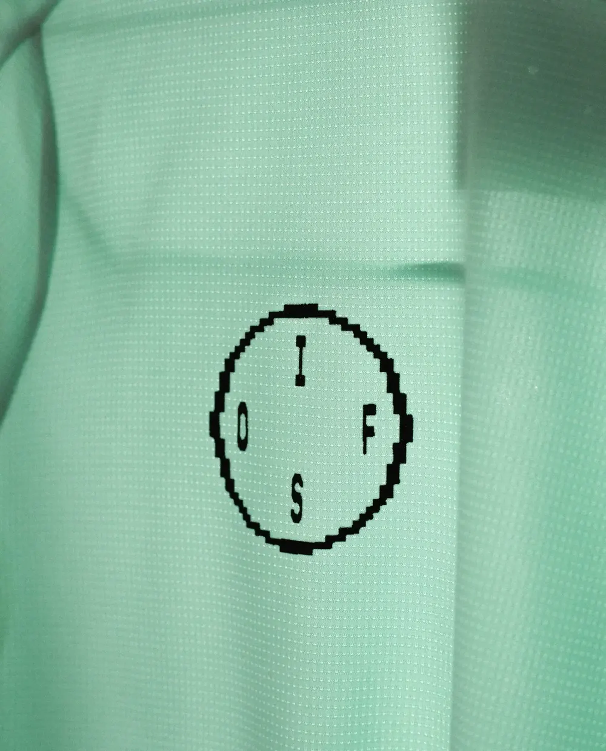 Close-up of a light green shirt with a black graphic oval with the letters I, F, S, and O arranged inside the oval.