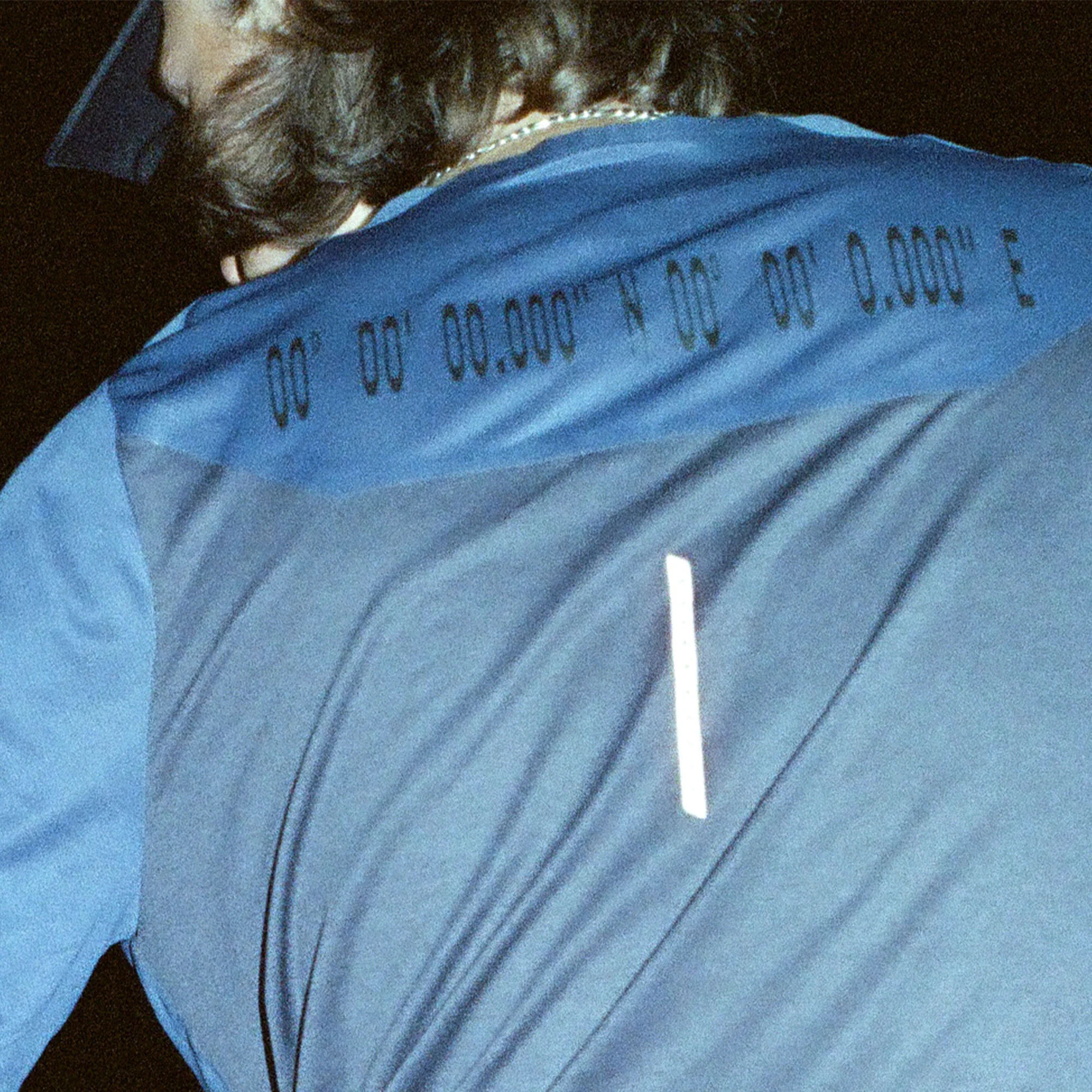 Close-up of a person wearing a blue athletic shirt featuring coordinates, showcasing sportswear and technical apparel details.