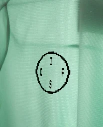 Close-up of textured mint green fabric featuring a black pixelated circular logo with letters arranged inside.