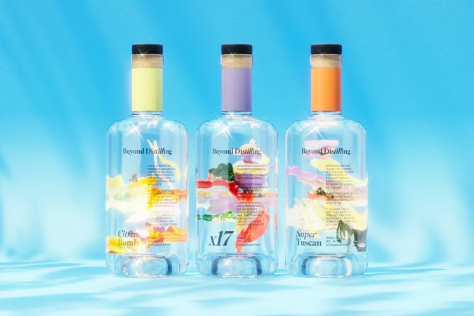 Three transparent bottles of Beyond Distilling spirits are showcased against a vibrant blue background with subtle lighting effects and colorful labels.
