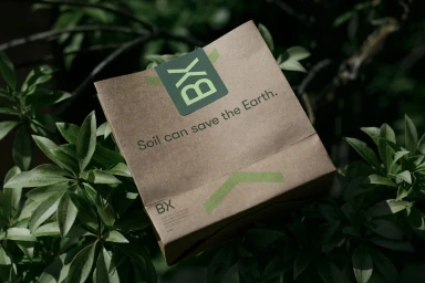 Brown paper packaging with green branding and text nestled amidst dark green foliage.