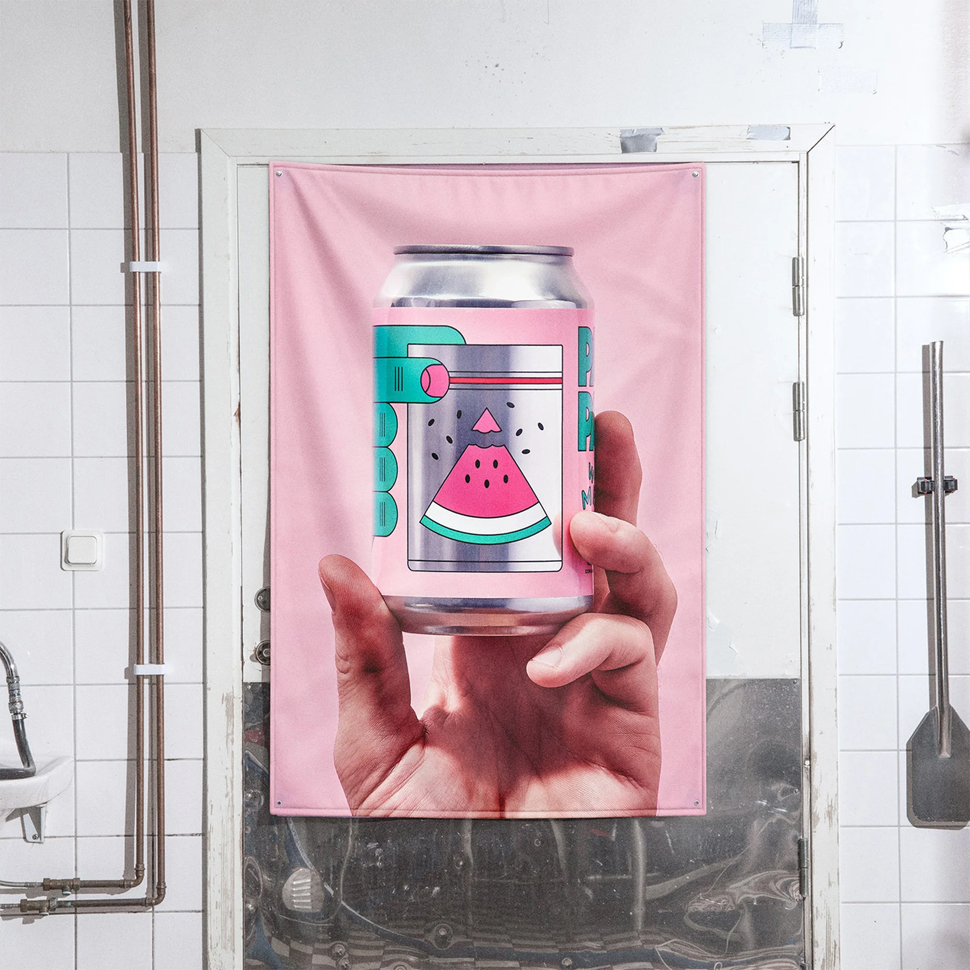 Graphic can of a watermelon drink held by a hand, depicted on a pink poster hanging on a white tiled wall with metal pipes.