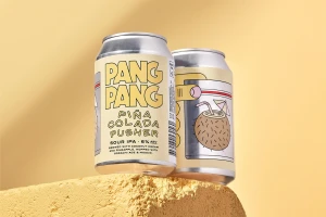 Two PangPang Pusher beer cans resting on a textured pale yellow stone block against a matching warm background.