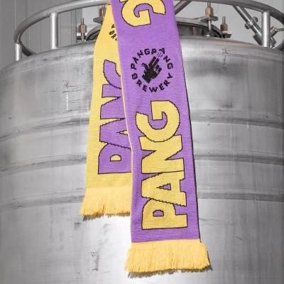 A knitted purple and yellow scarf featuring bold typography draped over a large industrial stainless steel tank.