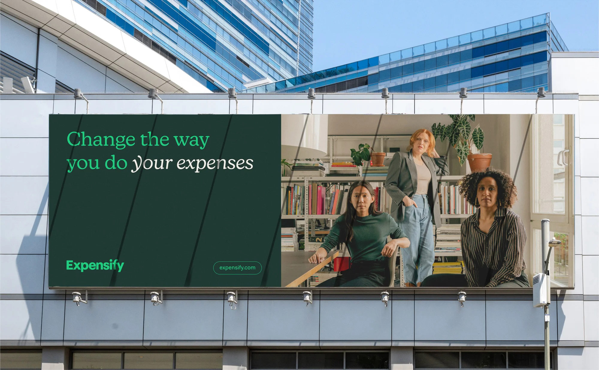 Billboard advertisement featuring three women posing in a well-lit setting, promoting expense management solutions with the brand 'Expensify'.