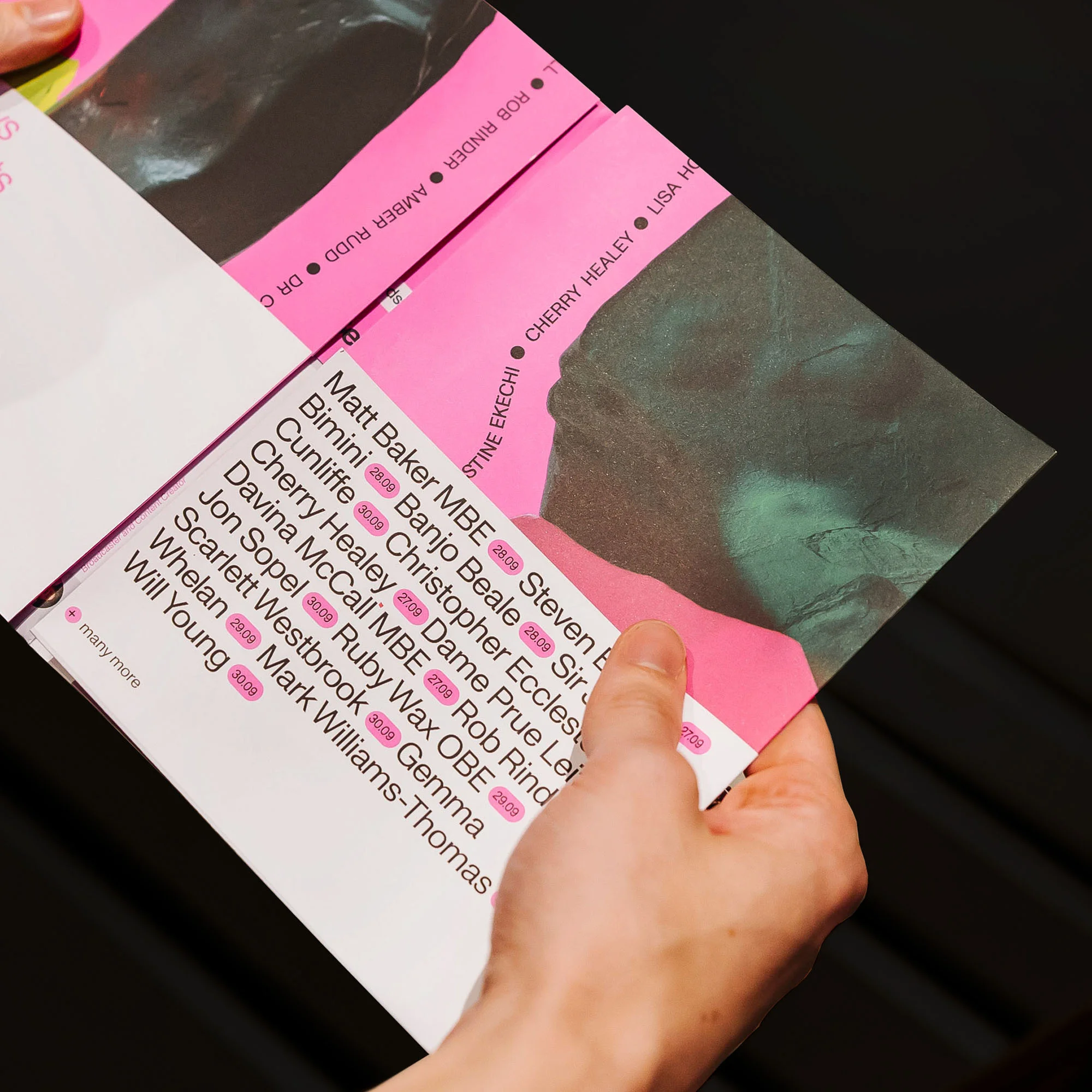 Hands holding a pink and white leaflet with names like Matt Baker MBE and Bimini printed on it. Part of a face illustration is also visible.