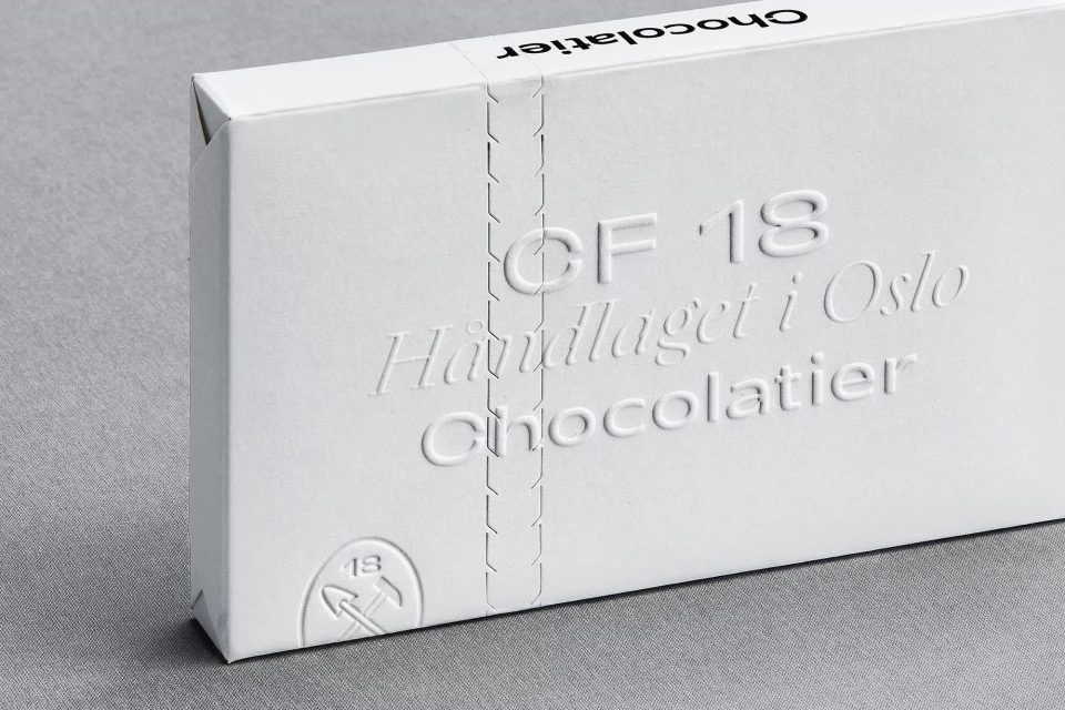 A close-up studio shot showcases an embossed white chocolate box with 'Chocolatier' text against a neutral grey backdrop.