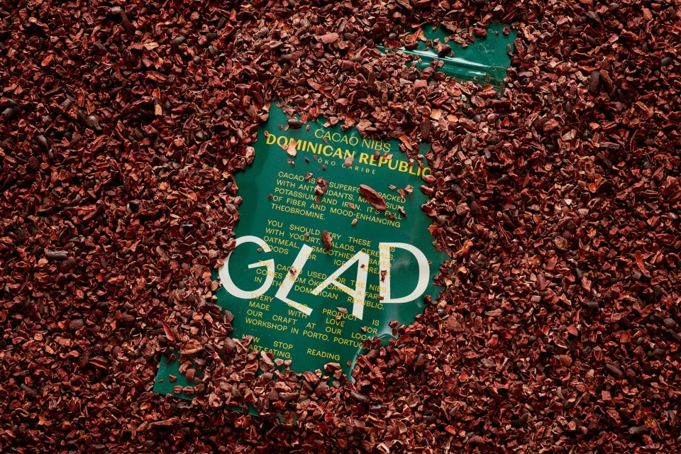 Cacao nibs from the Dominican Republic are scattered around a green package of Glad cacao nibs, showcasing a natural food product.