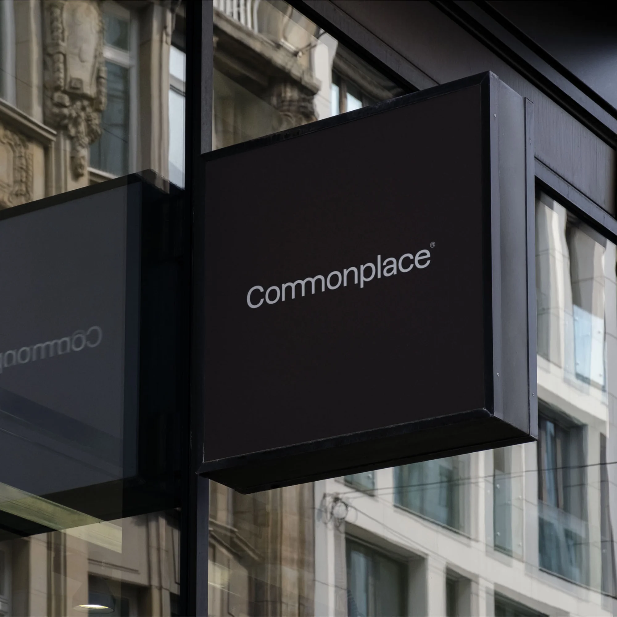 Black Commonplace sign attached to building exterior with windows and architectural details on a cloudy day, providing brand visibility.