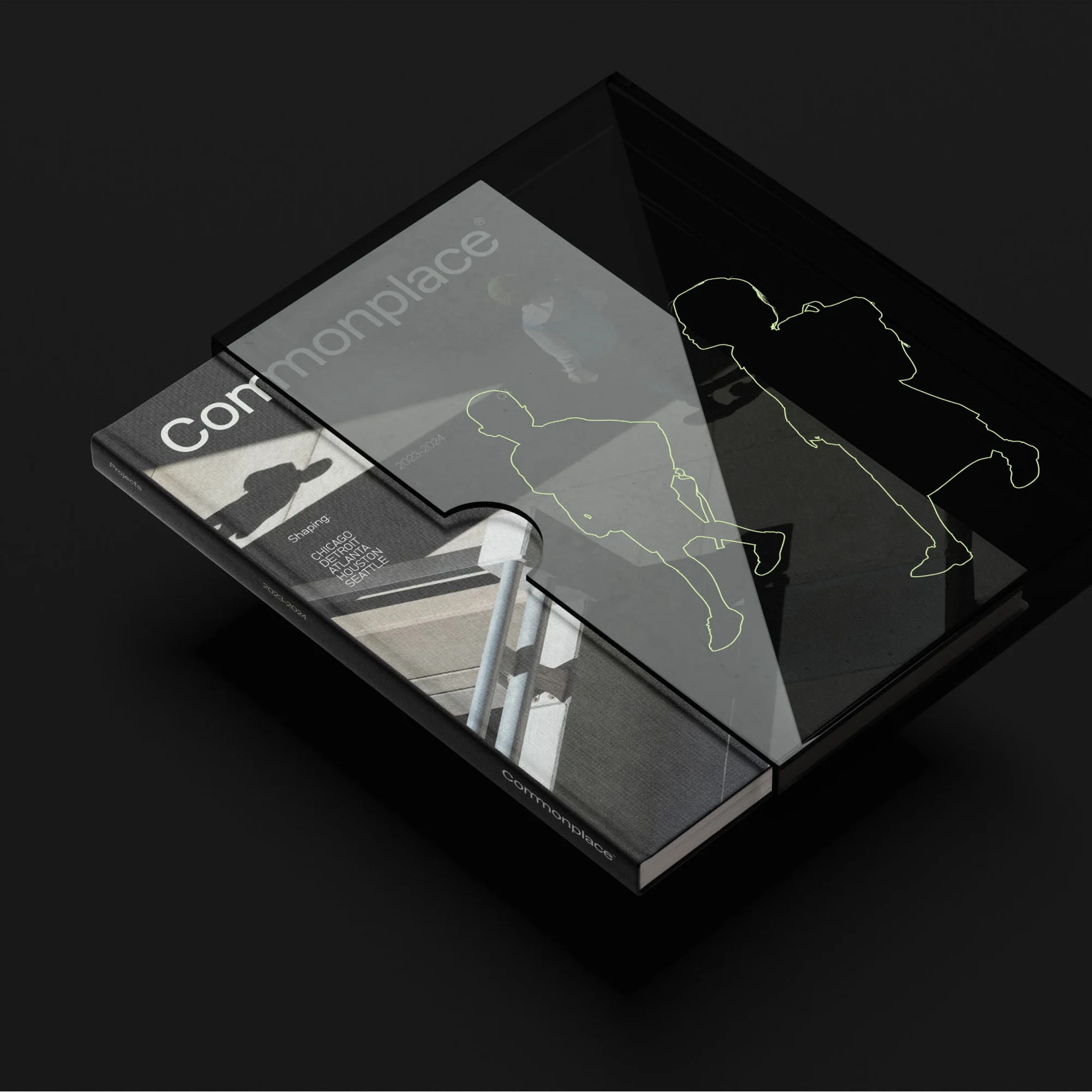 Overhead shot of a 'Commonplace' book and translucent puzzle piece on a dark surface, featuring building photography and figure outlines.