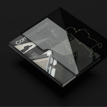 Overhead shot of a 'Commonplace' book and translucent puzzle piece on a dark surface, featuring building photography and figure outlines.