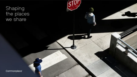 High angle urban street view showing two pedestrians walking past a stop sign casting long shadows on concrete pavement.