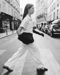Model walking across a city street wearing a light-coloured jumpsuit and black gloves, captured by Claudia Smith.