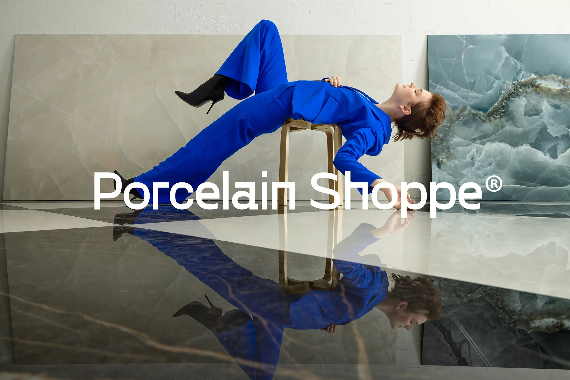 Woman in blue suit and heels posing on a stool in front of a glossy floor and stone-look panels, modern and stylish product shot.