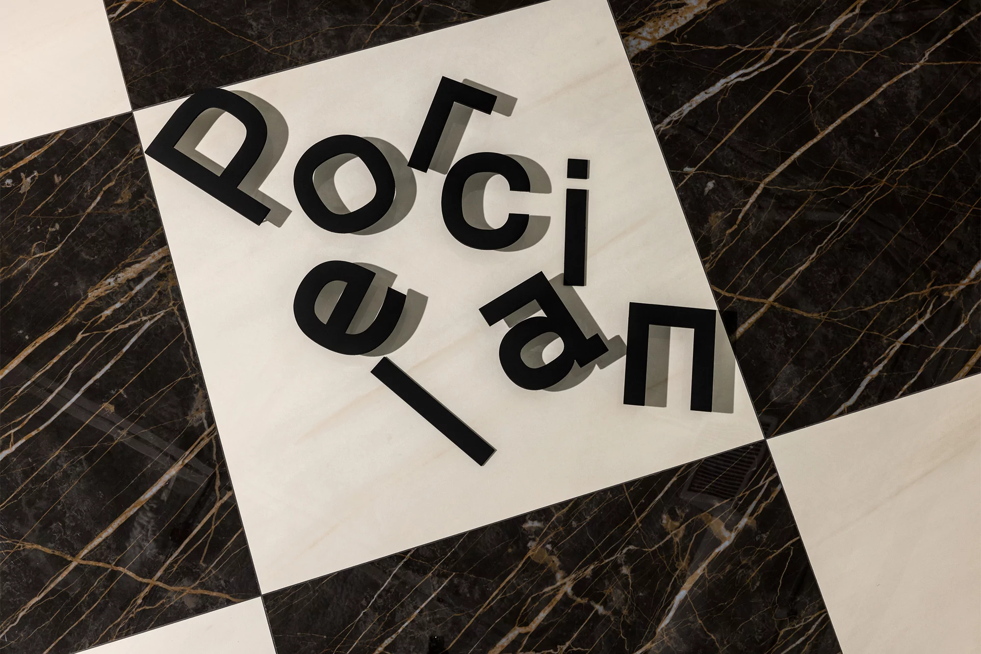 Overhead view of black letter cutouts spelling 'Porcelain' on a floor with black and white marble tiles, arranged on a white tile.