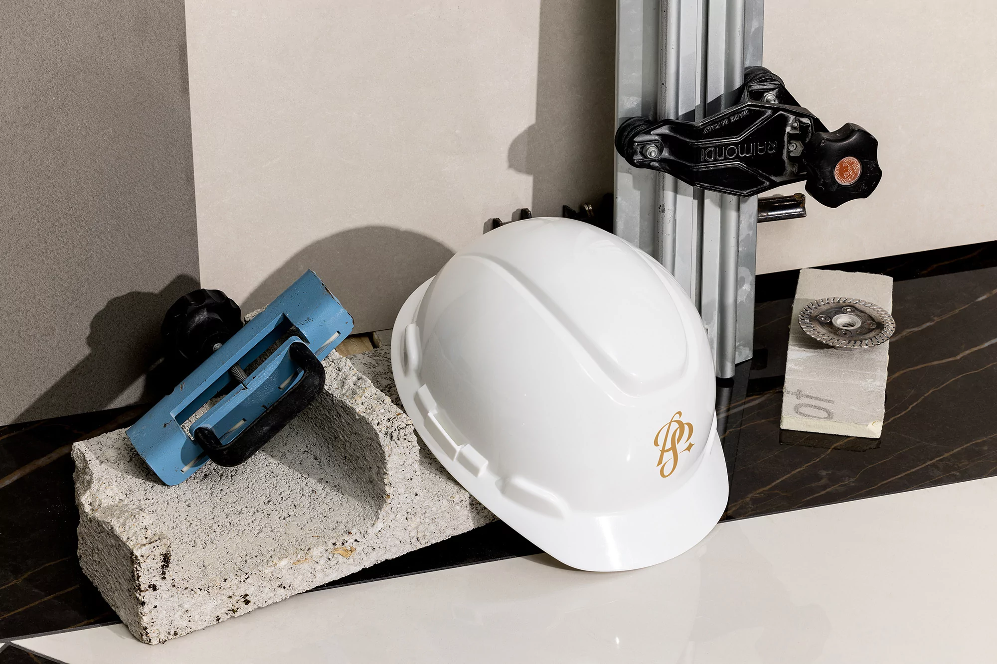 A construction scene featuring a white hard hat, a tile cutter, and tiling tools against a background of grey and black tiles.