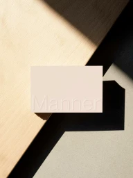Beige business card with debossed Manner logo resting on wooden and stone surfaces casting diagonal shadows.