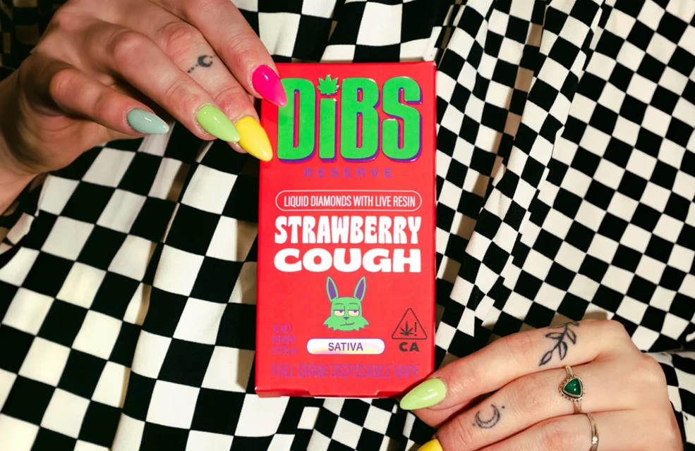 Close-up of a person holding a red 'Dibs Reserve Strawberry Cough' product box against a black-and-white checkered background.