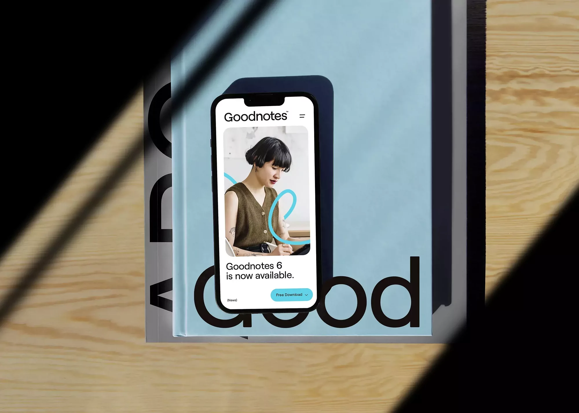 Goodnotes app shown on mobile phone screen placed on book and table with shadow; modern design and technology concept.
