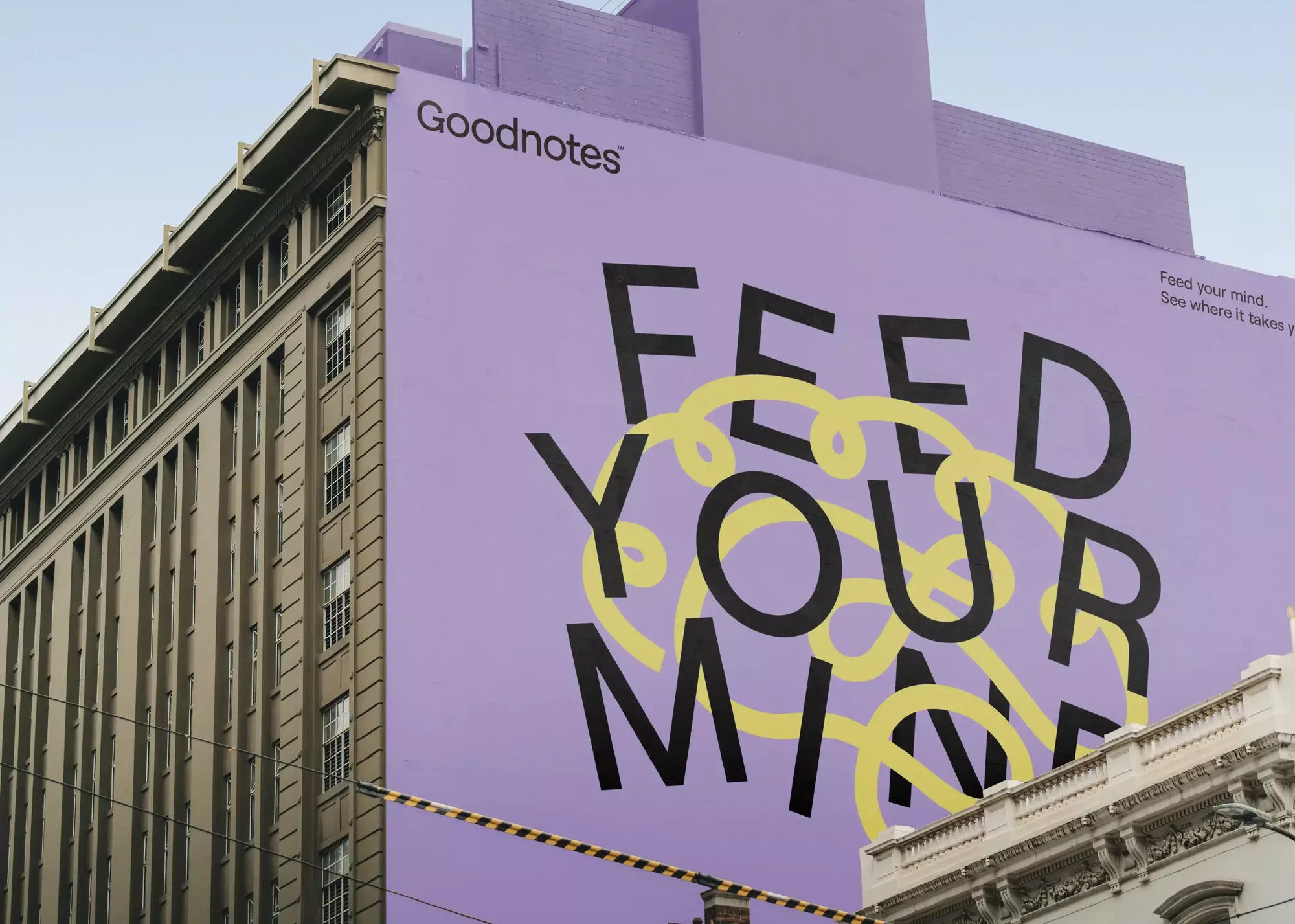 Large Goodnotes ad on the side of a building with the text 'Feed Your Mind' in black and yellow on a purple background.