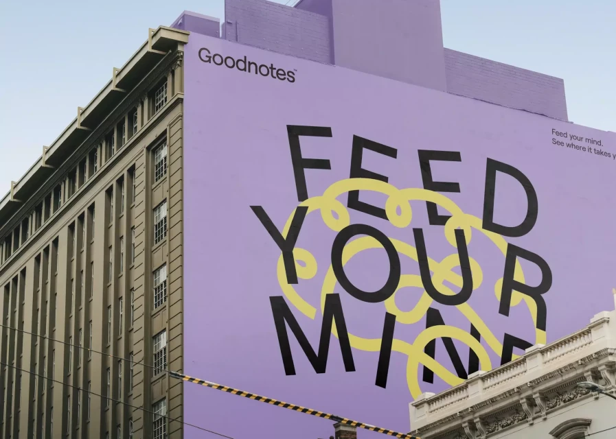 Large Goodnotes ad on the side of a building with the text 'Feed Your Mind' in black and yellow on a purple background.