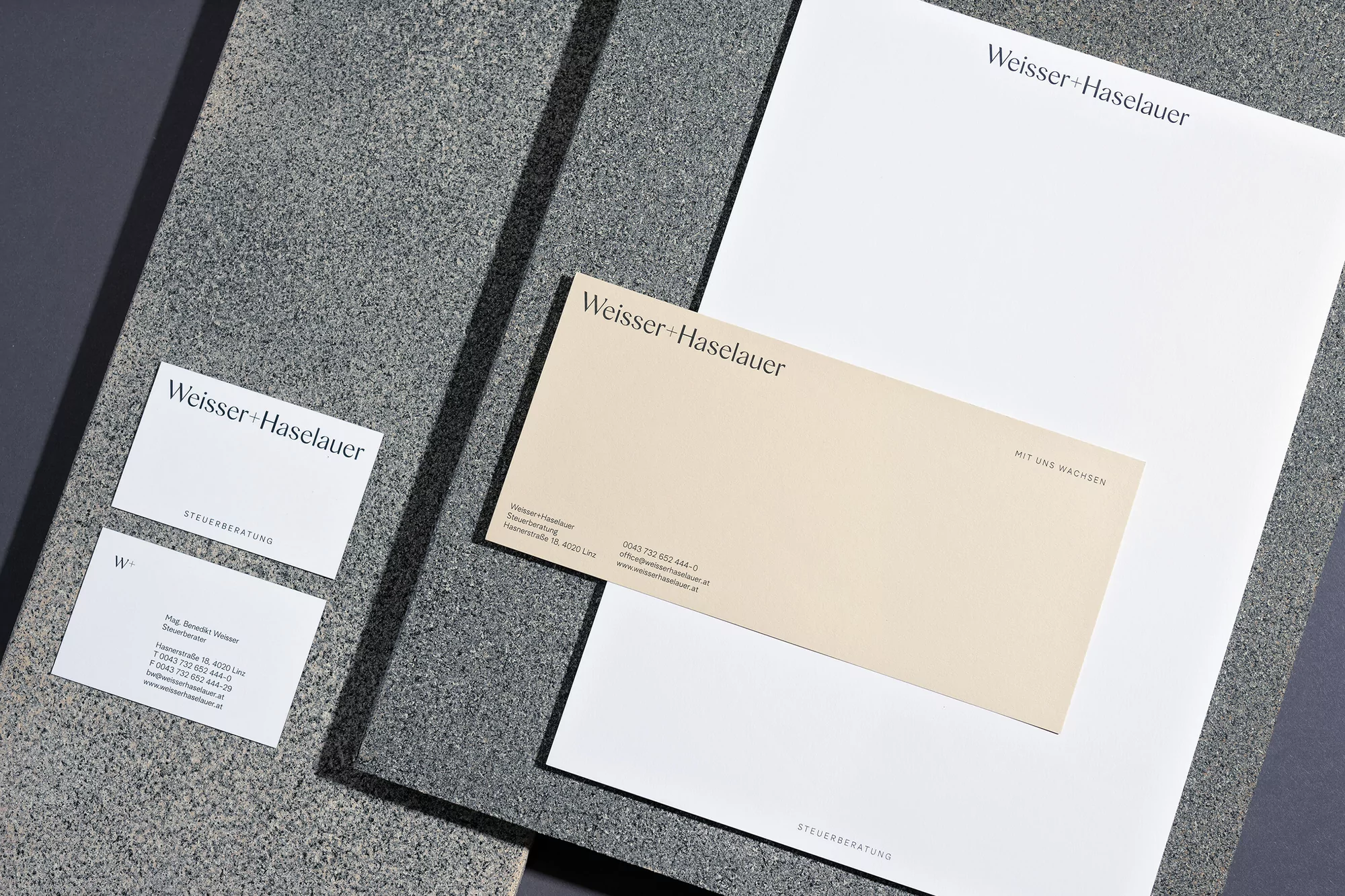Close-up of Weisser + Haselauer branded stationery: business cards, letterhead, and envelope on a textured gray surface.