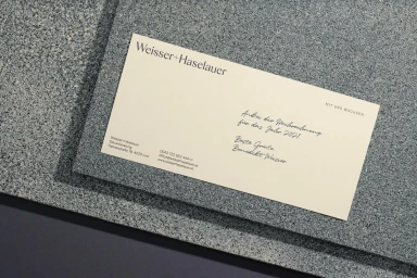 Cream-colored branded letterhead stationery resting on a textured grey granite stone surface with sharp shadows.