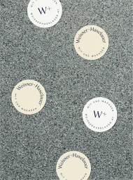 Round white branded stickers featuring dark typography scattered across a textured grey speckled stone surface.
