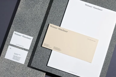 Weisser Haselauer brand identity stationery set featuring letterhead, envelopes, and business cards on textured stone surface.