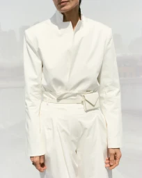Model in white high neck jacket with matching trousers and small belt bag against light background