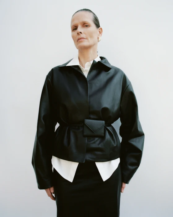 Model wearing a black leather jacket over a white shirt against a white background for St Agni.