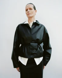 Model wearing a black leather jacket over a white shirt against a white background for St Agni.