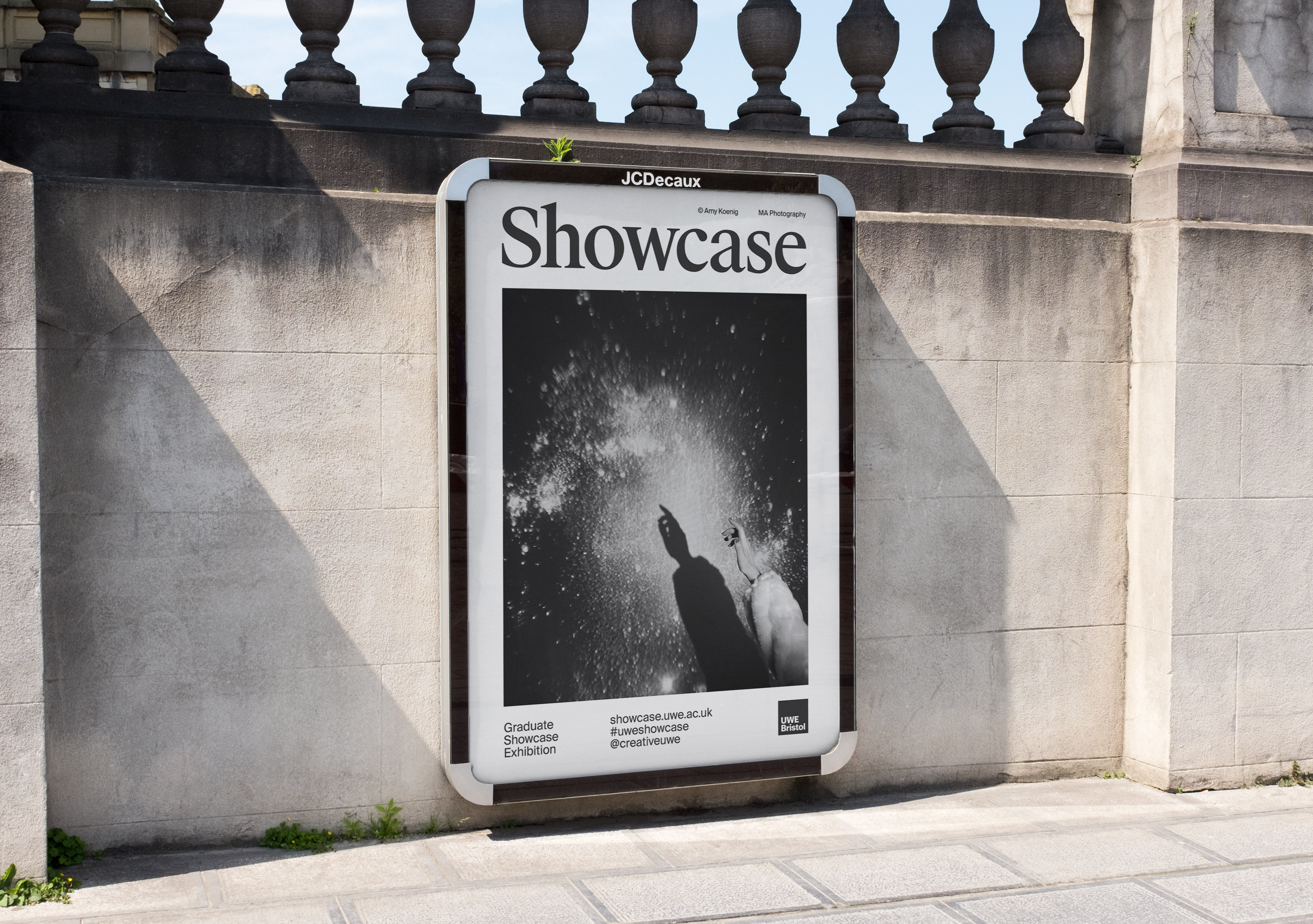 Outdoor advertising billboard showcasing monochrome photography on a stone wall with classic balustrade under bright natural light.