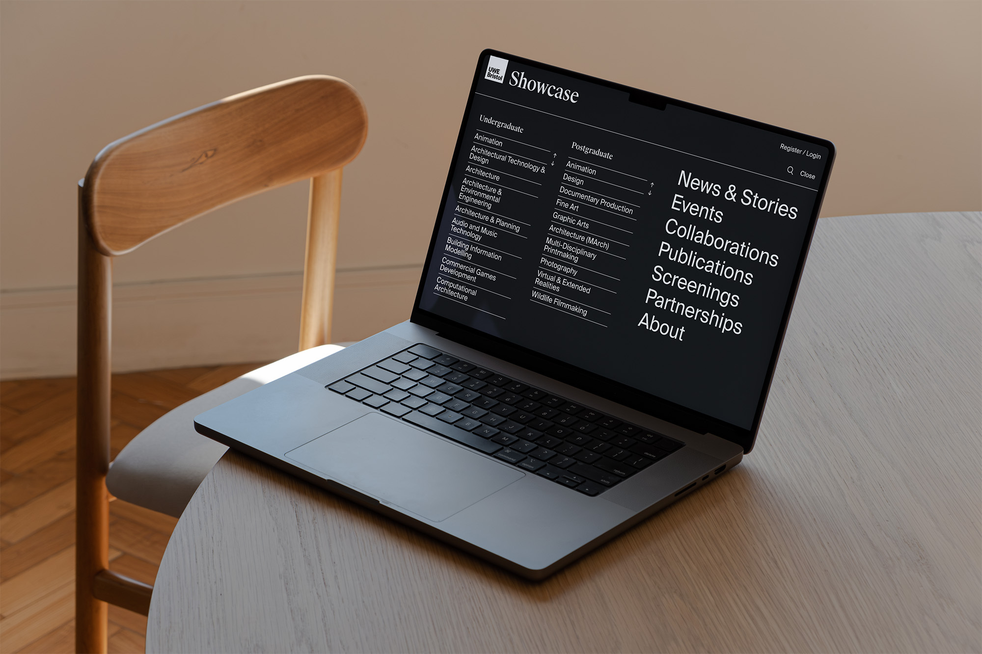 Laptop on a wooden table next to a chair, displaying a showcase website with text about architecture, design, and photography.