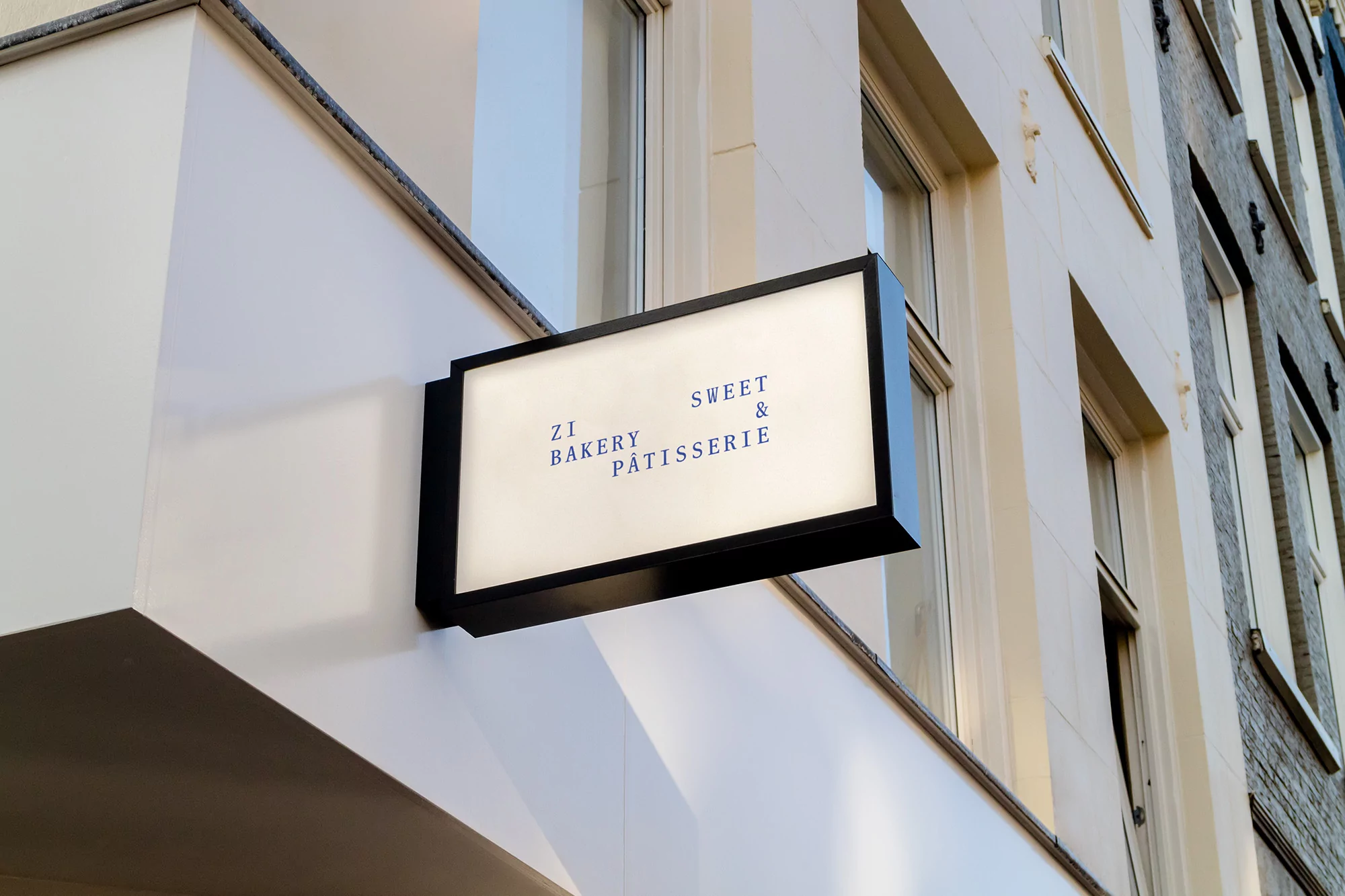 Exterior view of a bakery sign with the text 'ZI Bakery Sweet & Patisserie', mounted on a white building with multiple windows.