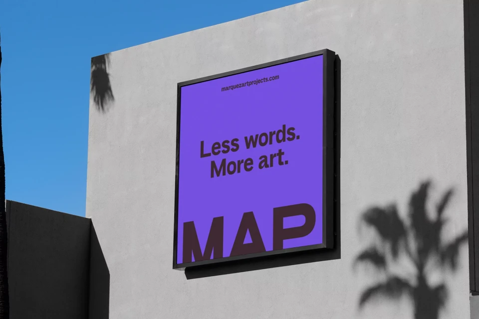 Purple and brown framed artwork mounted on a grey wall with shadows from palm trees on a sunny day with a blue sky.