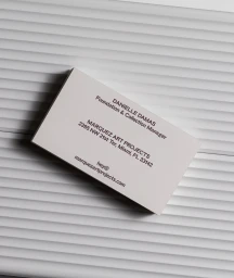 A stacked business card featuring black typography on a white textured card resting on a corrugated surface